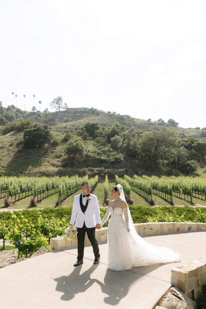 Bride and groom walking through vineyard at romantic San Diego wedding venue